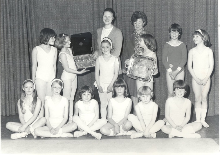 A black and white photograph of Miss Aitchison and Mrs Walker surrounded by teenage students. One of which is holding a largs silver award.